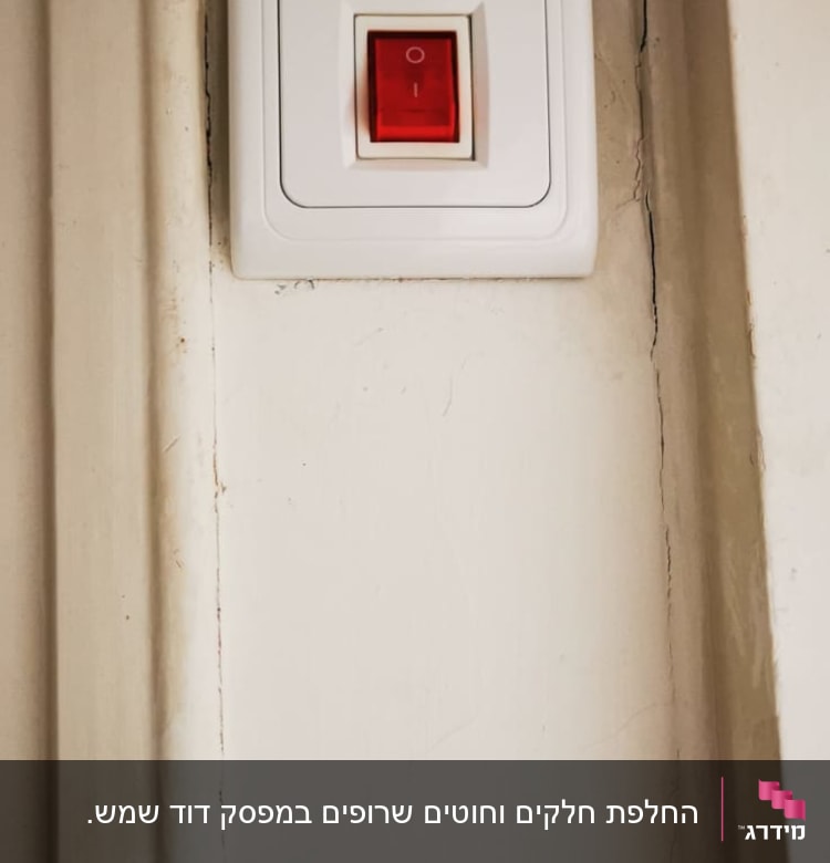 מתג חשמלי עם כפתור אדום על קיר לבן